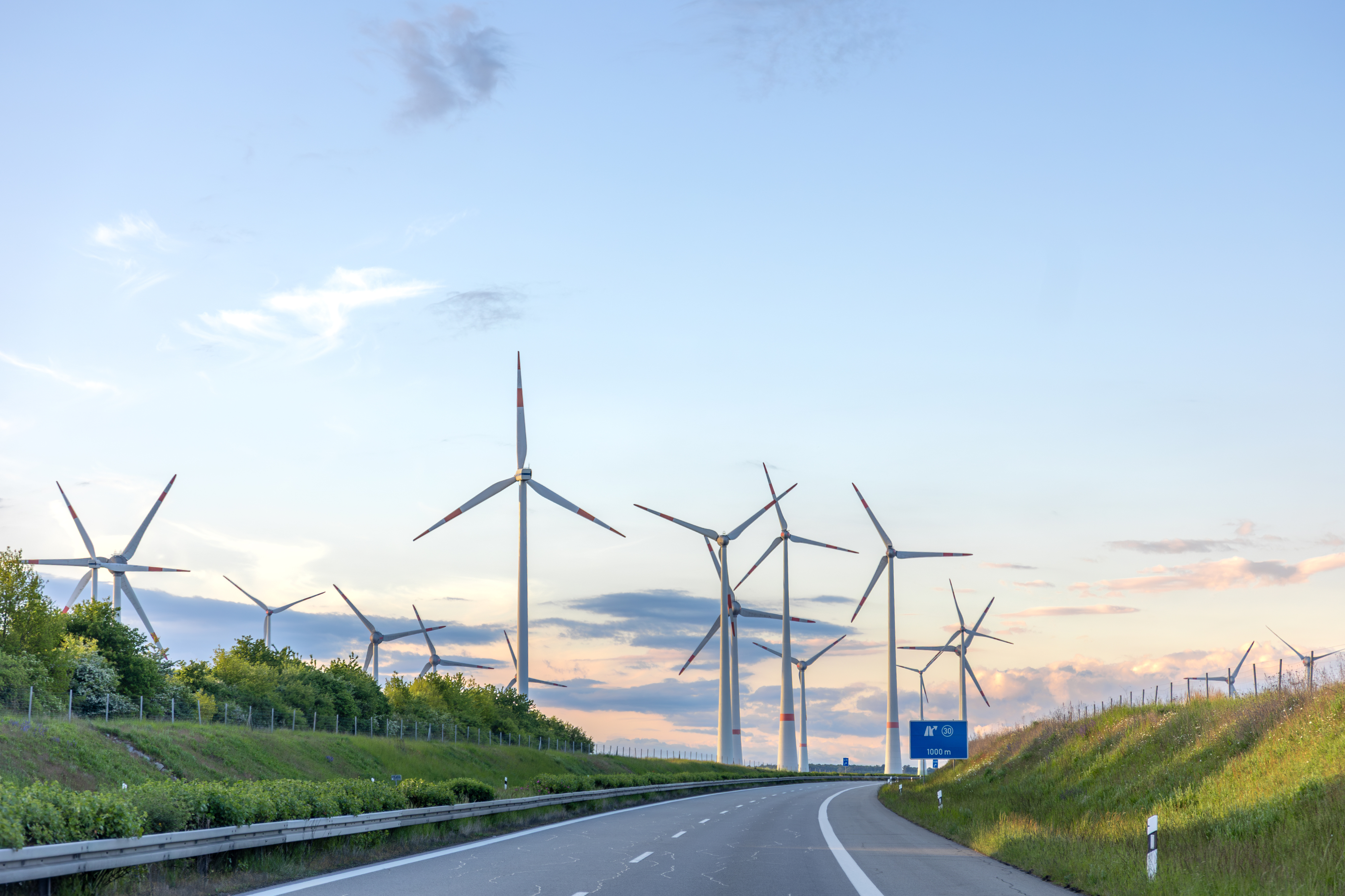 Wind turbines by a road at sunset